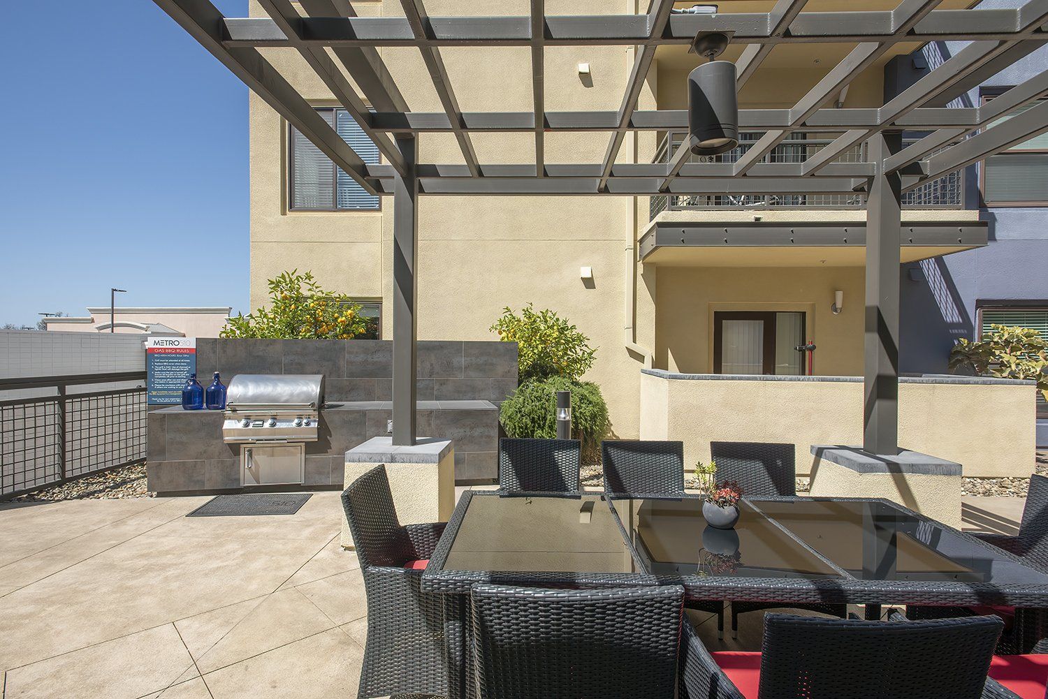 El Cerrito, CA, Apartments - Metro 510 - BBQ Area with Grilling Station and Dining Table with Chairs Under Pergola.