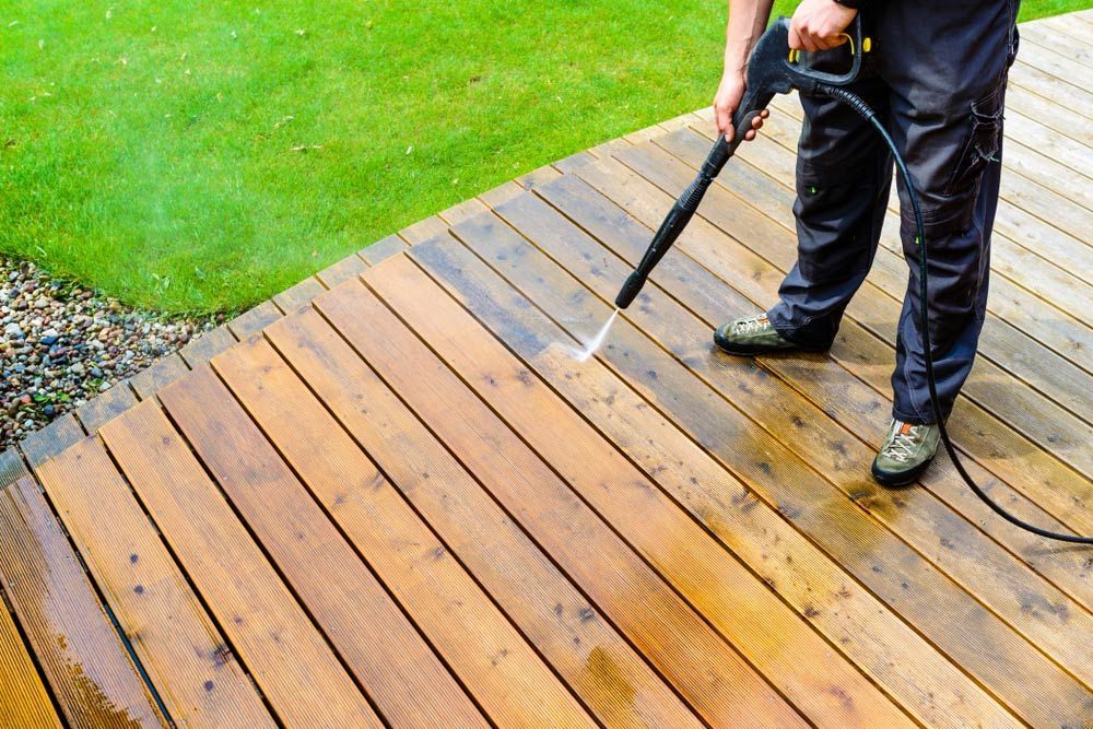 A Man is Cleaning a Wooden Deck With a High Pressure Washer — Tony Eldridge Property Services in Forster, NSW