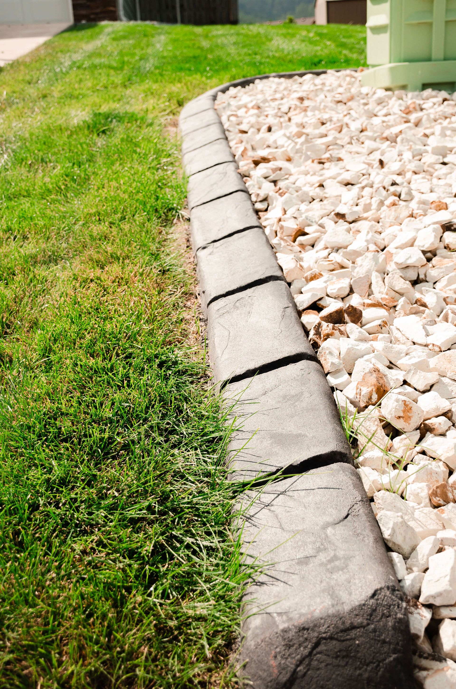 A concrete curb surrounds a lush green lawn next to a pile of gravel.