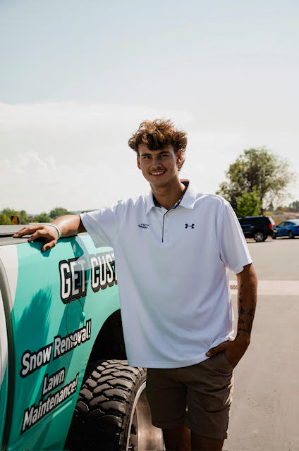 A young man in a white shirt is standing next to a truck.
