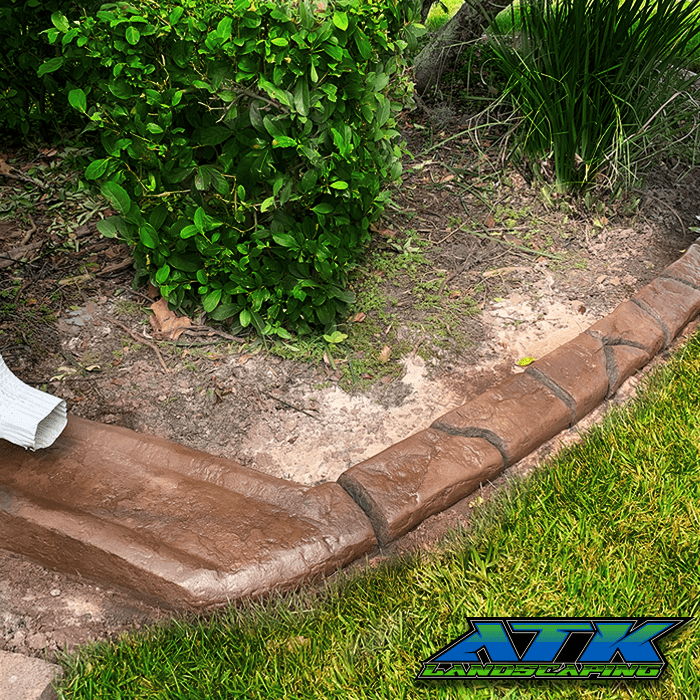 A drain pipe is sitting next to a concrete curb in a garden.
