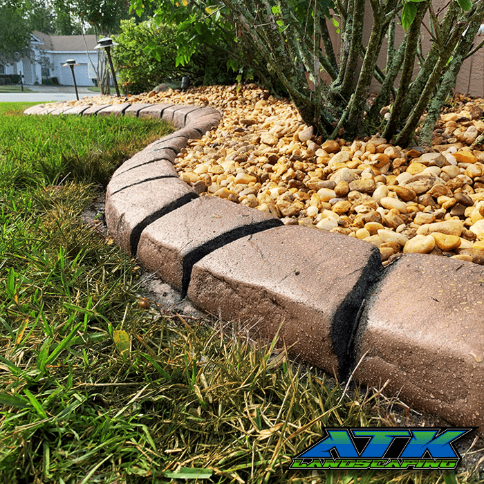 A concrete curb is surrounded by rocks and grass in a yard.
