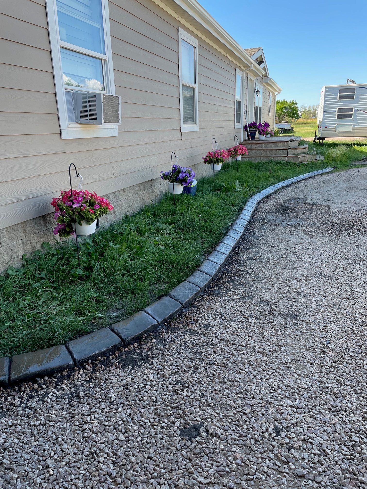 A house with a gravel driveway and flowers in front of it.
