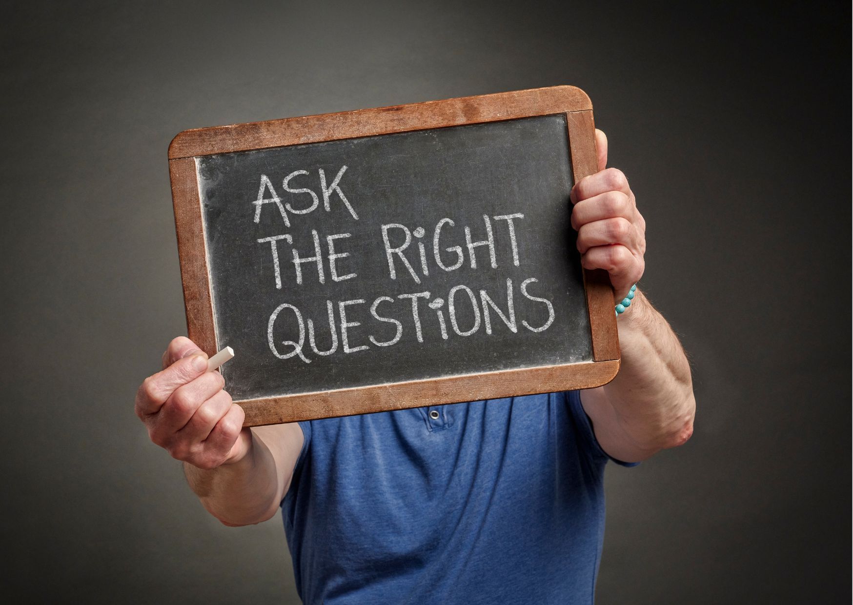 Person holding chalkboard sign reading ask the right questions for real estate guidance concept.