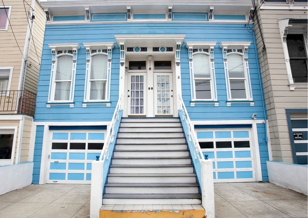 Vibrant turquoise Victorian townhouse with white stairs, twin entrances, garage doors below, and decorative window frames in San Francisco style.