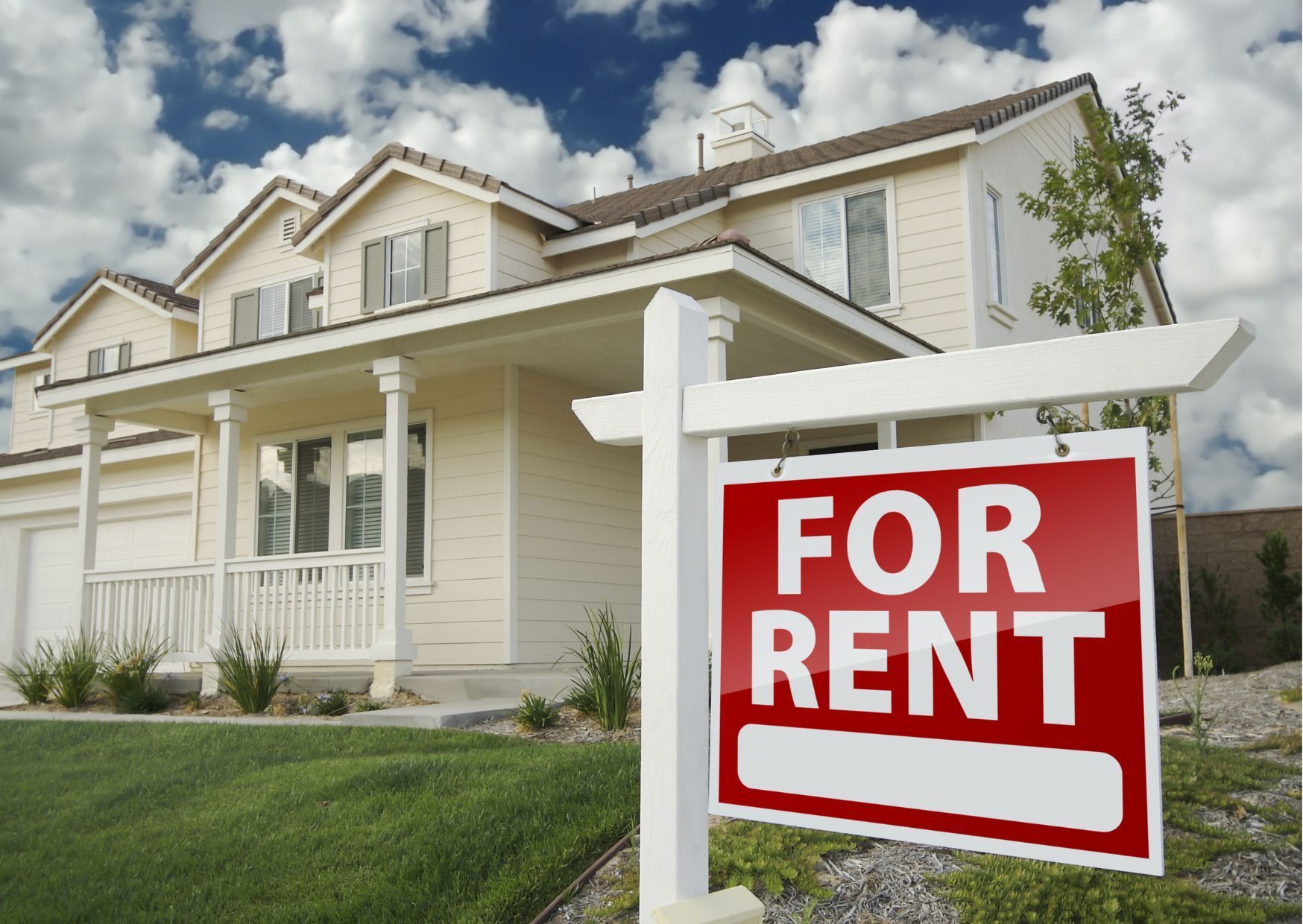Suburban home with large red for rent sign on front lawn under sunny blue sky.