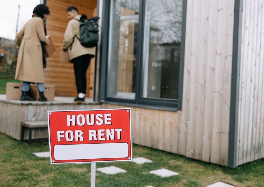 People viewing a rental home beside a for rent sign, emphasizing property verification before payment.