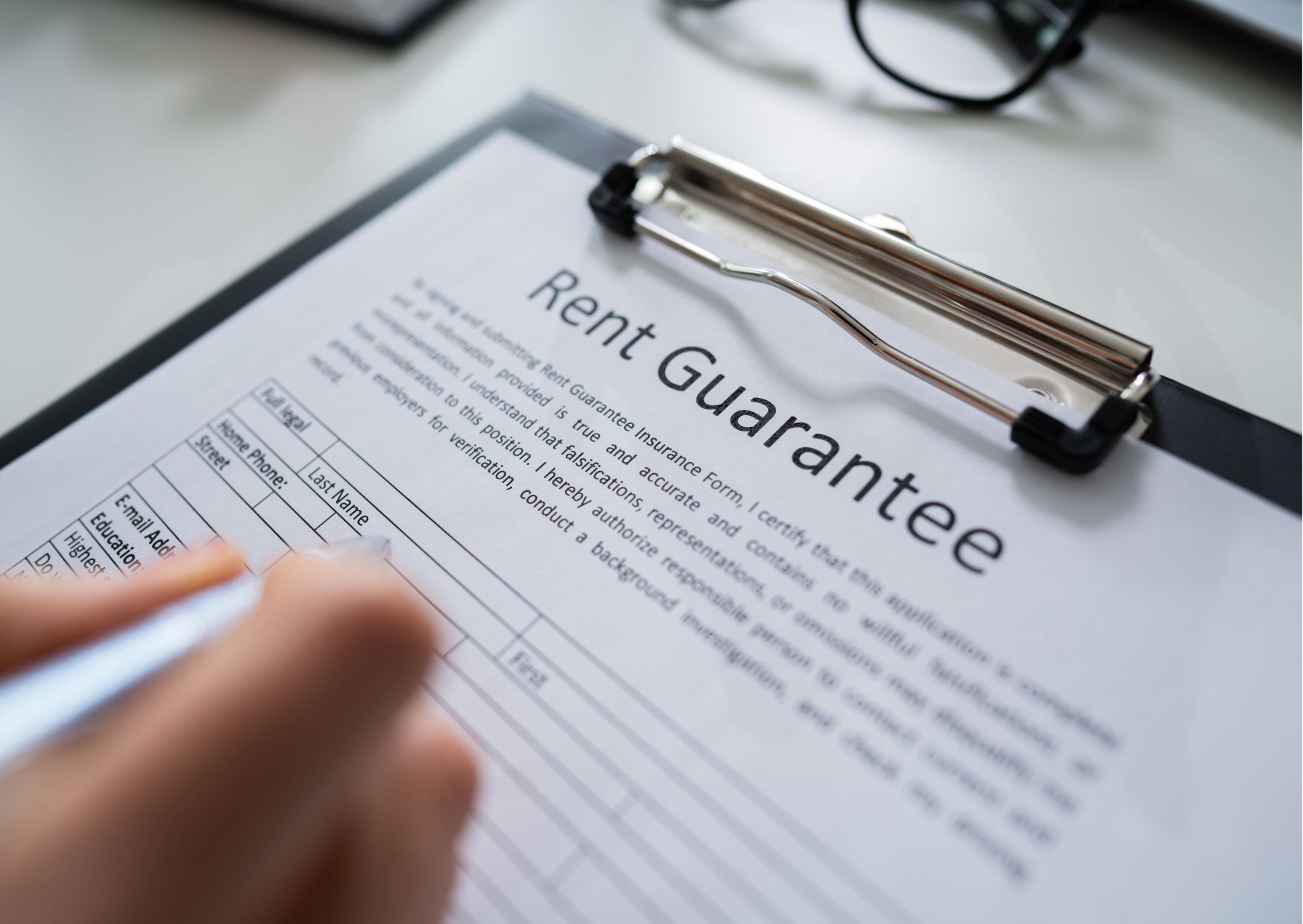 Hand reviewing rent guarantee contract on clipboard representing rental agreement security and tenant protection.