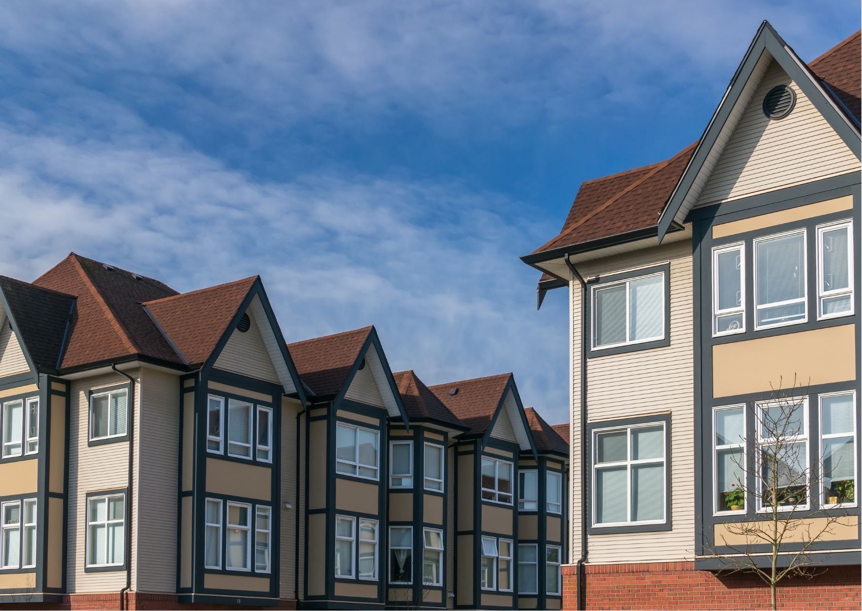 Modern townhouses with peaked roofs and beige siding lined up in a residential neighborhood under blue sky.