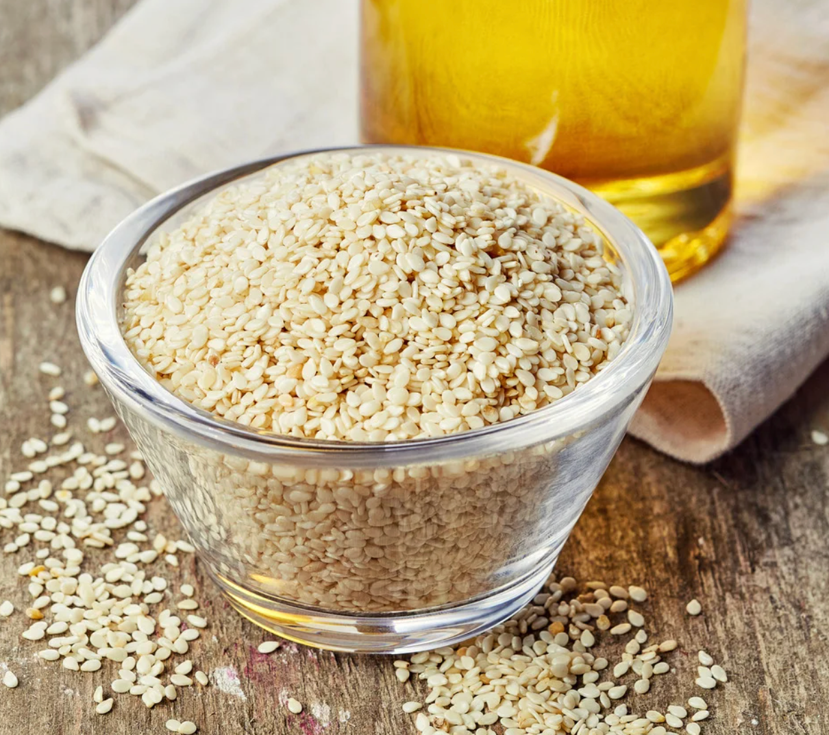 Bowl of sesame seeds with a bottle of oil on a wooden surface.