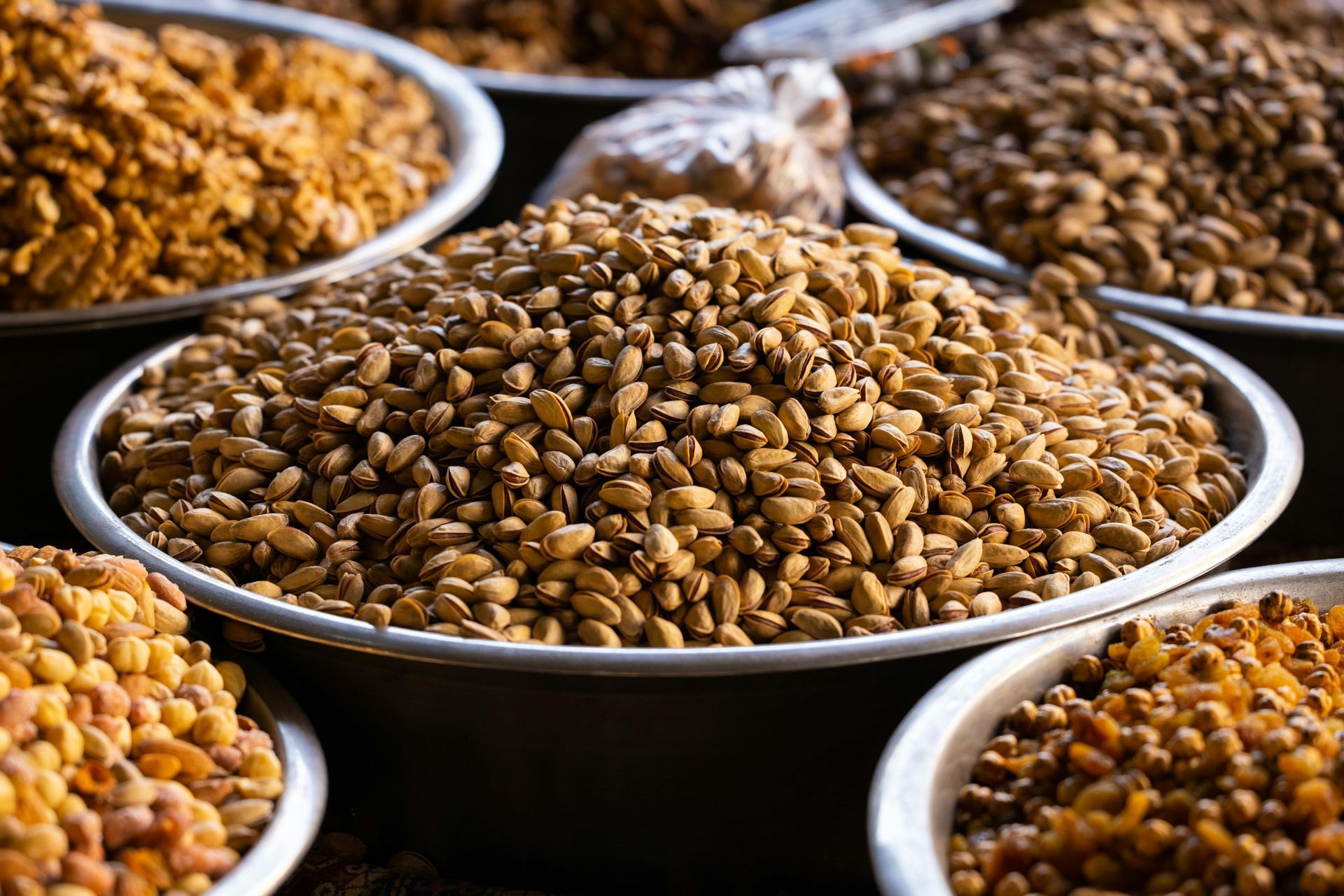 Bowls of assorted nuts, including pistachios and other seeds, at a market.