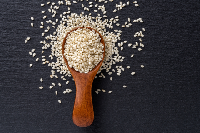 Sesame seeds in a wooden spoon, spilling onto a dark surface.