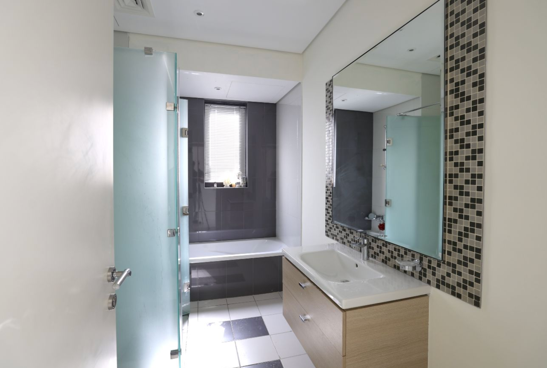 Modern bathroom with frosted glass shower door, vanity with a rectangular mirror, and a window.
