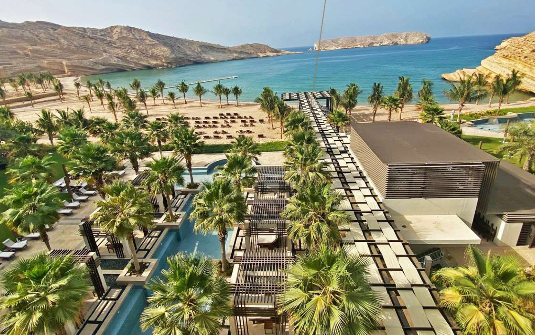 Beach resort with palm trees, turquoise water, and mountains in the background.