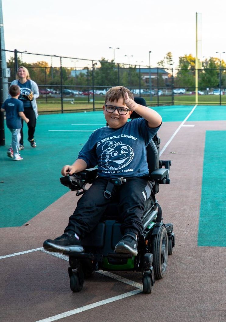 A young boy is sitting in a wheelchair on a tennis court.
