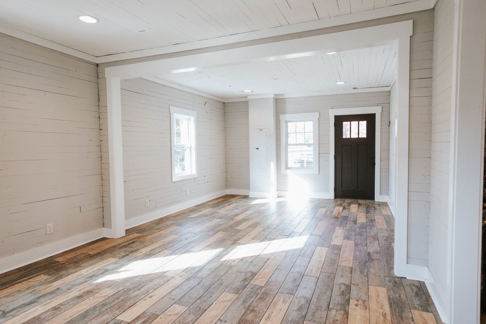 An empty living room with hardwood floors and a black door.
