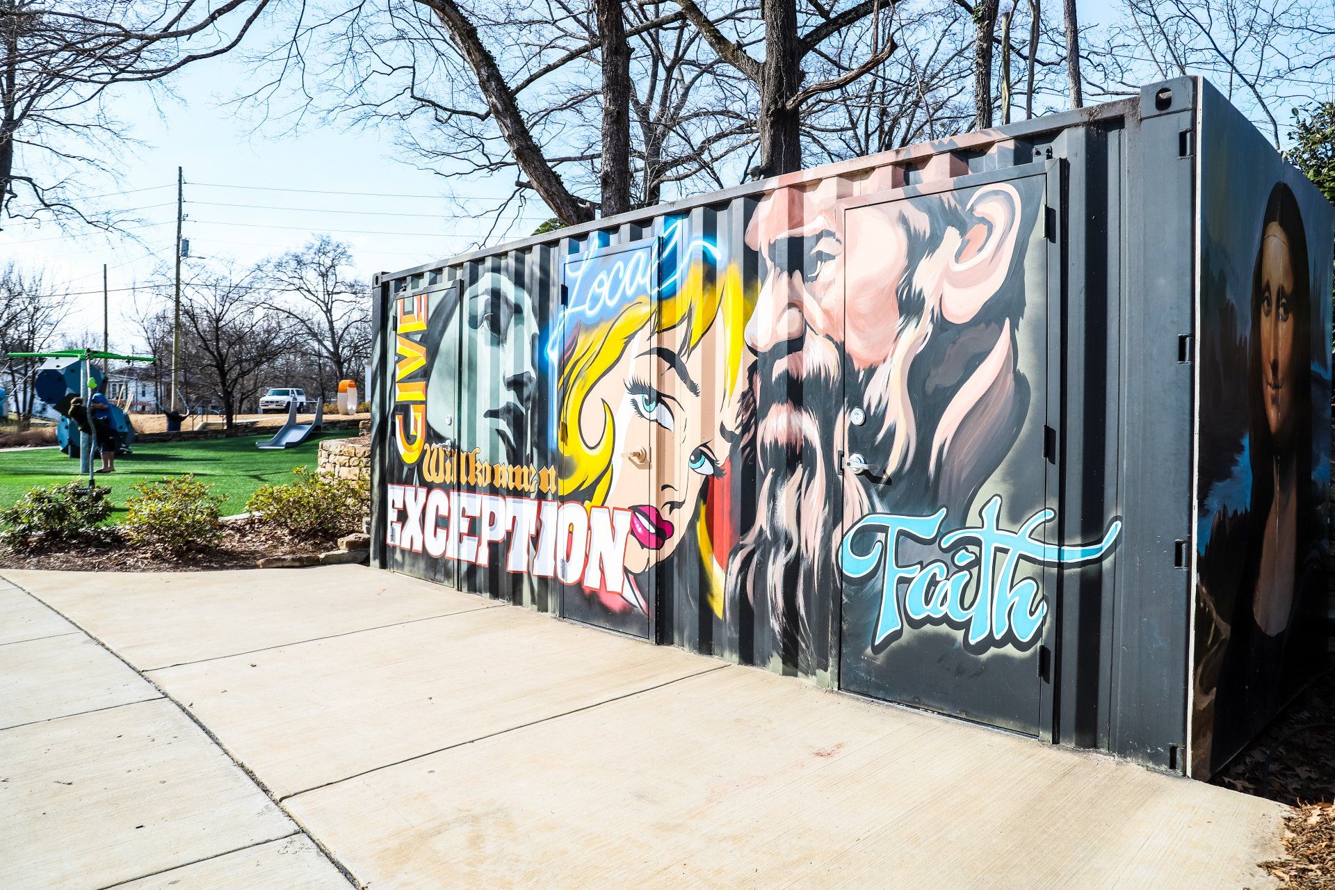 A container with graffiti on it and a playground in the background.