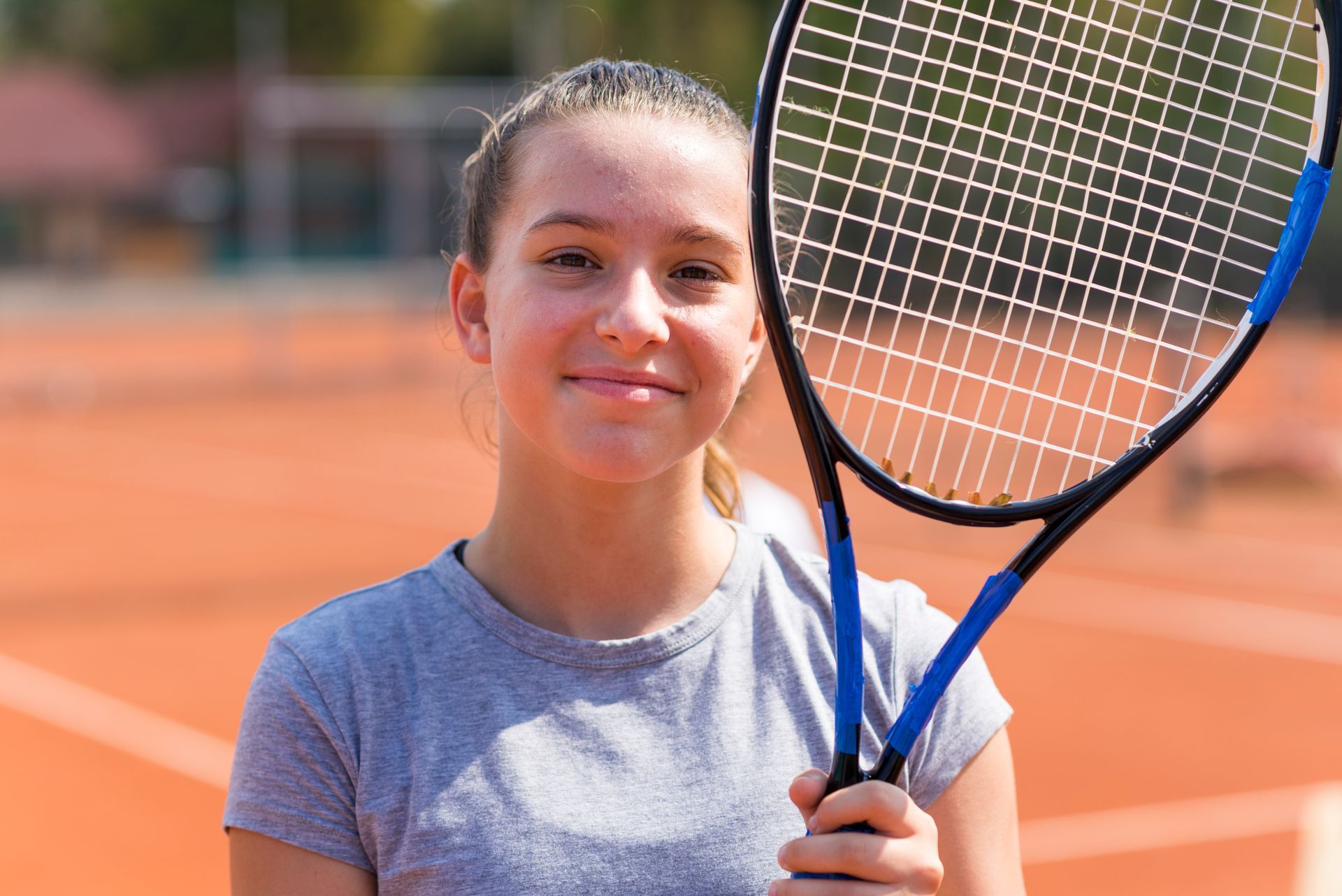 A young girl is holding a tennis racquet on a tennis court.