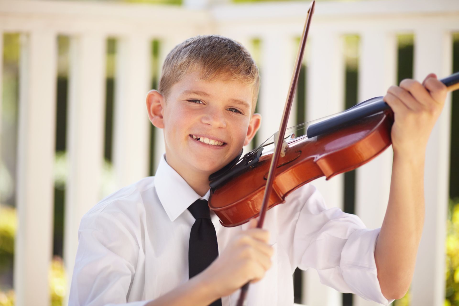 A young boy in a white shirt and black tie is playing a violin.