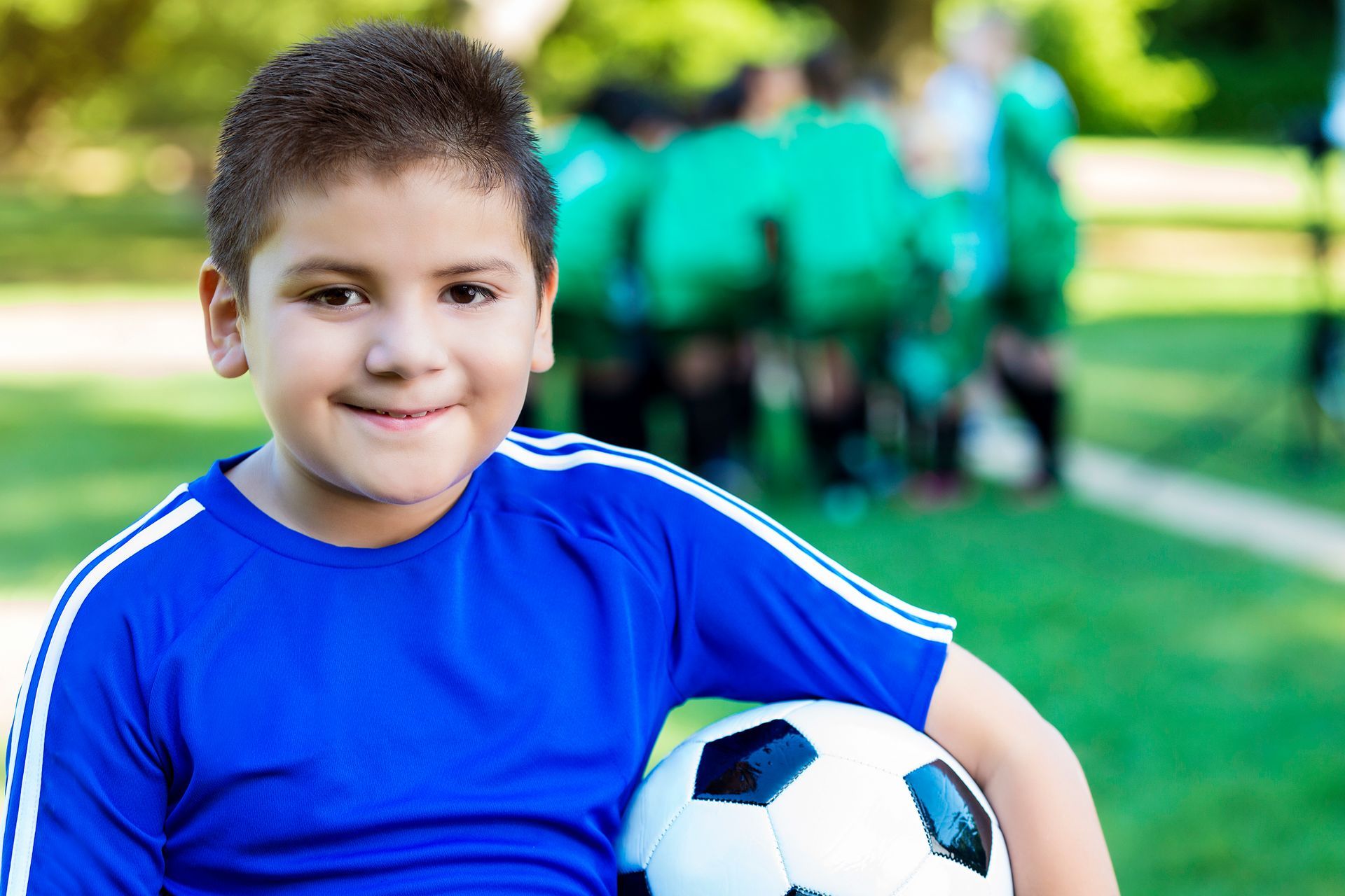 A young boy in a blue shirt is holding a soccer ball