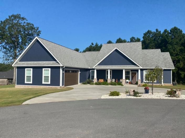 Single-story blue house with a gray roof, front porch, and curved driveway under a clear sky
