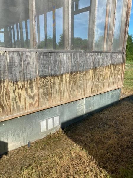 Weathered wooden wall with screened windows on a grassy exterior building side.