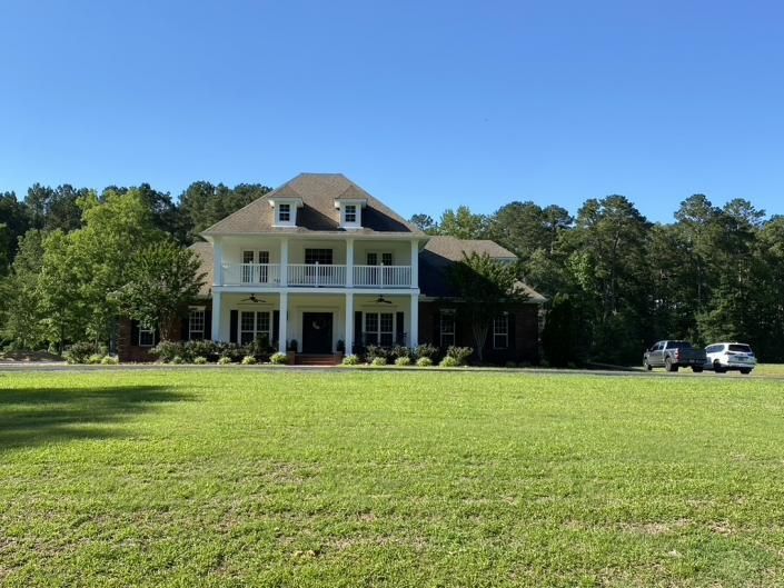 Large white house with tall columns and a wide green lawn under a clear blue sky