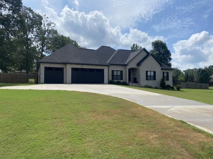 Single-story beige house with dark roof, three-car garage, and curved driveway on a grassy lot.