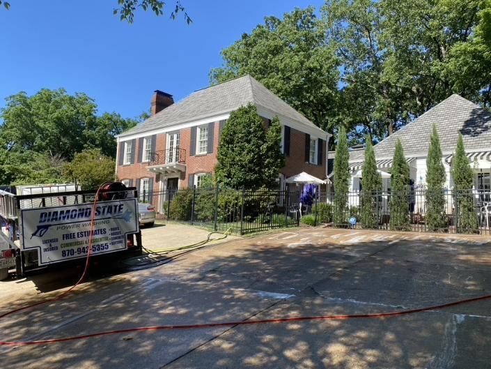 Brick house with white shutters, a tented side yard, and a truck parked by a driveway under blue sky
