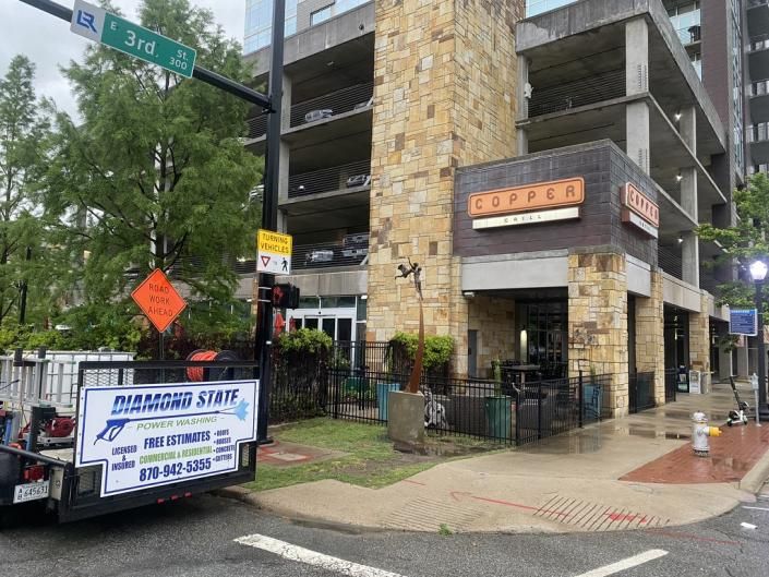 Street corner with a multi-story parking garage, sidewalk storefront, and a sign for a moving truck rental.