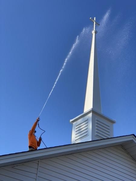 Worker spraying water onto a white church steeple against a blue sky