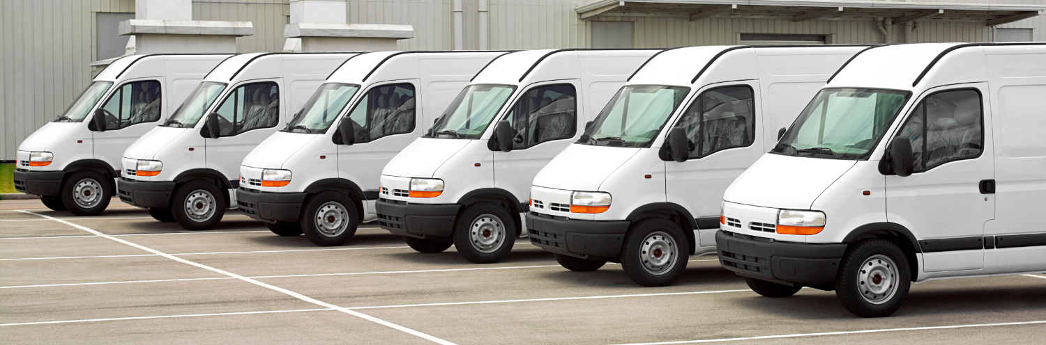 Line of white delivery vans parked in front of a warehouse