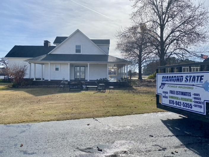 White house with porch and winter yard beside a blue moving dumpster on a driveway.