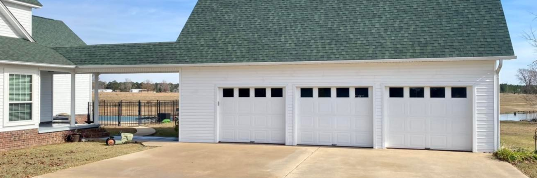 White house exterior with a green roof and three-car garage on a paved driveway.