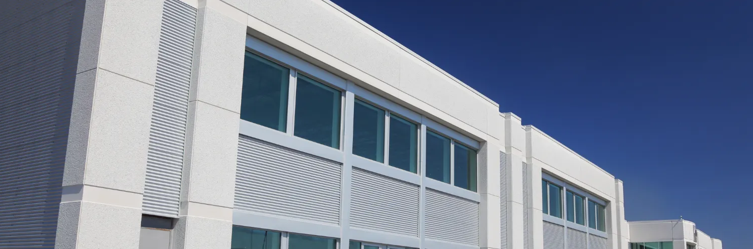 Modern white building facade with blue-tinted windows under a clear blue sky
