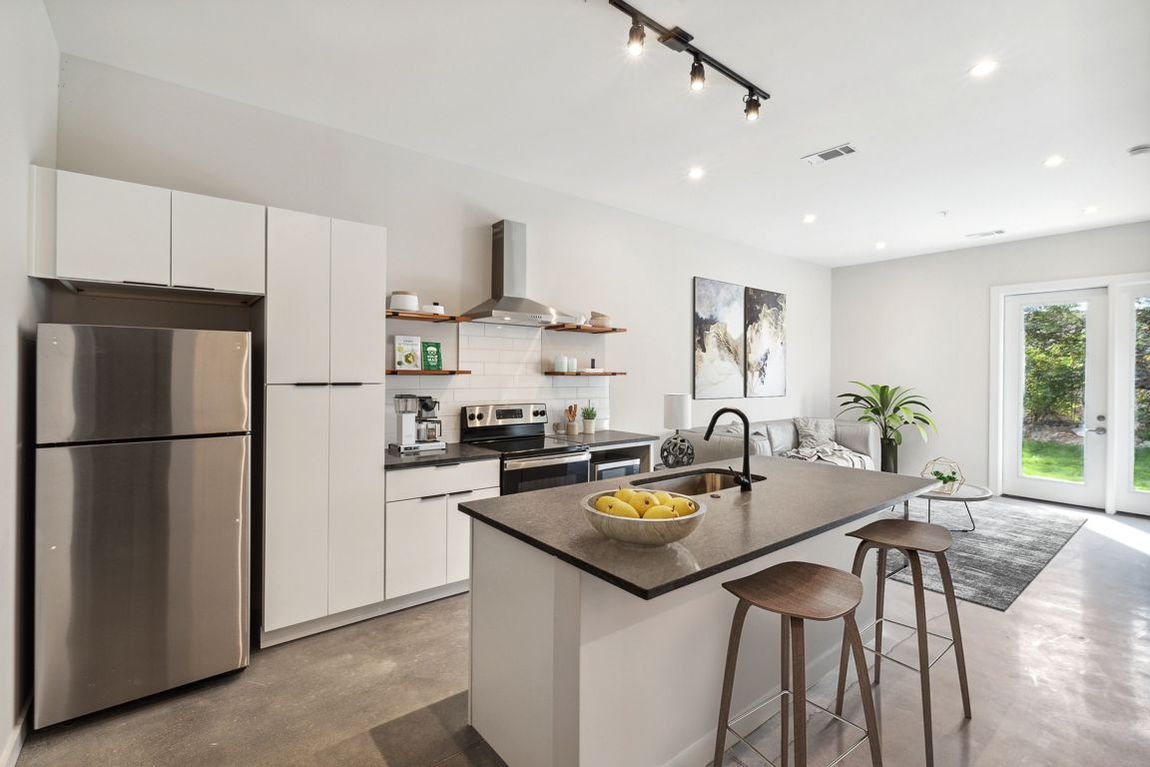 Modern kitchen with stainless steel appliances, island with stools, and open to a living area with patio doors.