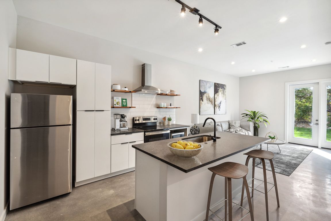Modern kitchen with stainless steel appliances, island with stools, and open to a living area with patio doors.