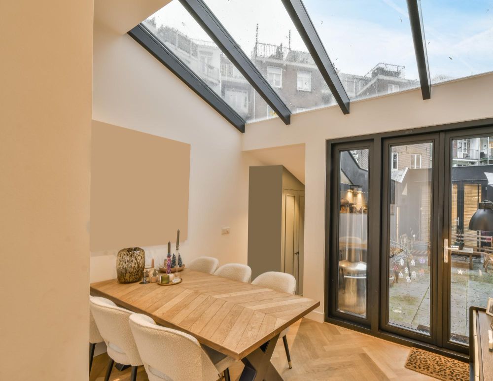 Bright dining room with a wooden table, white chairs, and glass doors under slanted skylights