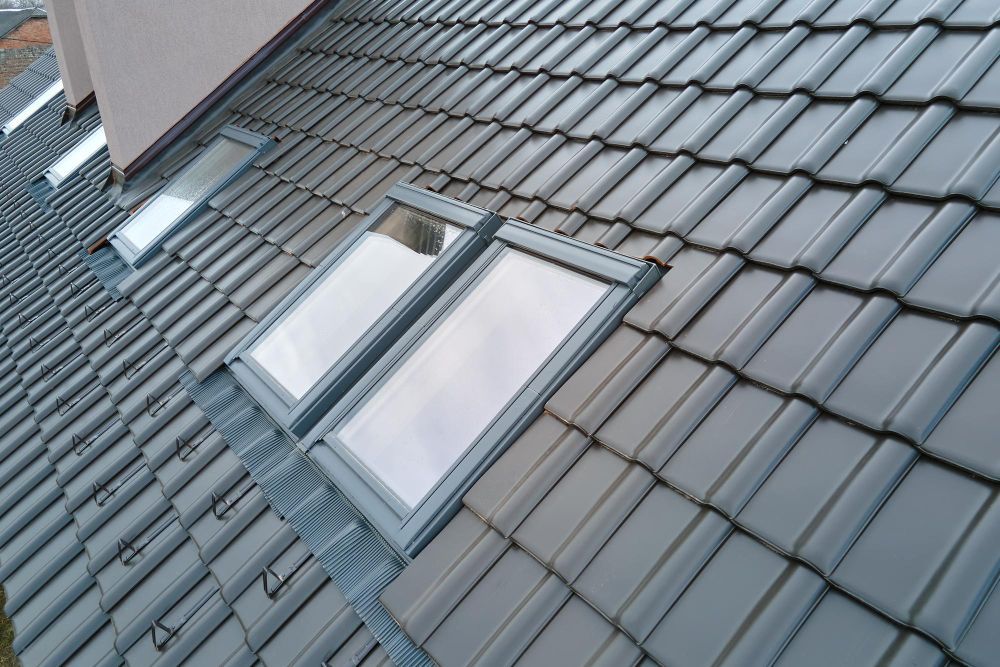 Two skylights on a gray tiled roof beside a brick building