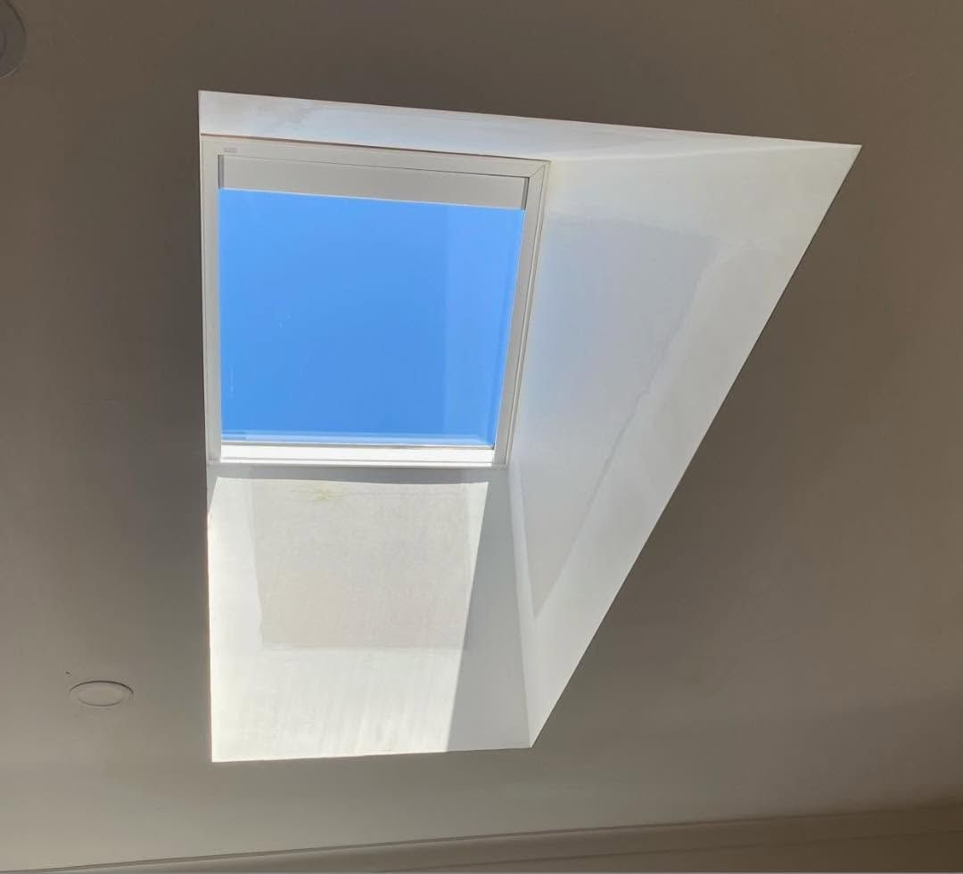 Open skylight in a white ceiling with blue sky visible above.