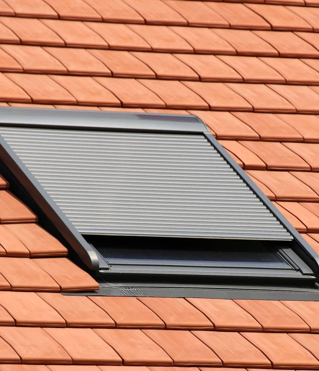 Open roof window with gray shutter on a red tiled roof
