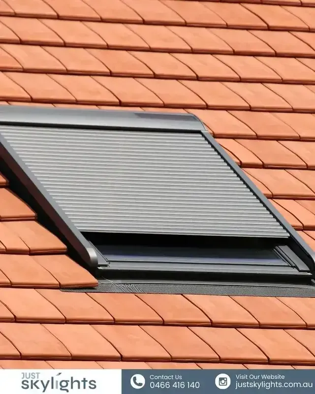 Tilted skylight window with a closed gray blind on a red tiled roof