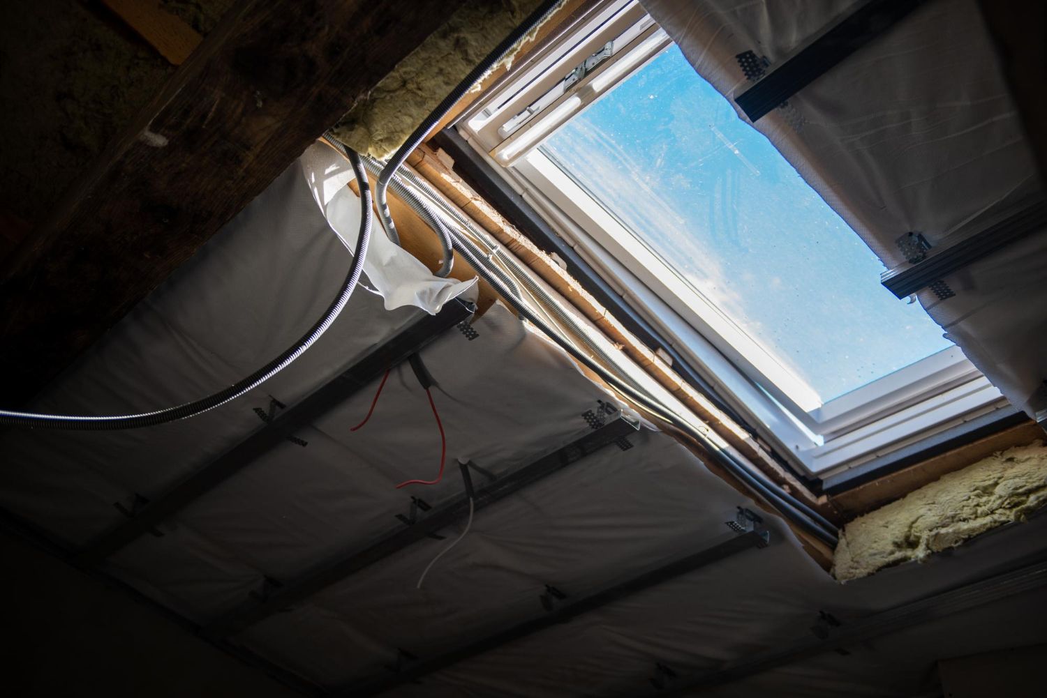 Damaged attic ceiling with exposed insulation and a skylight showing blue sky