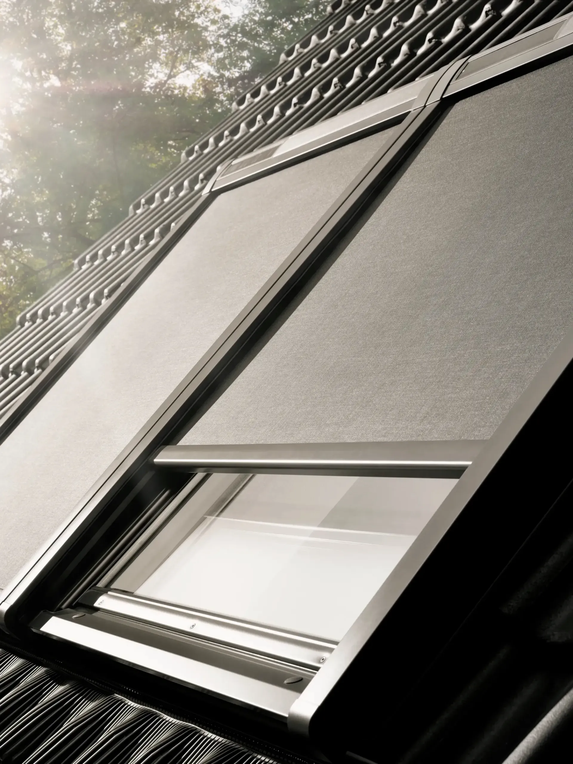 Open skylight window on a slanted roof, with sunlight and trees reflecting on the glass.