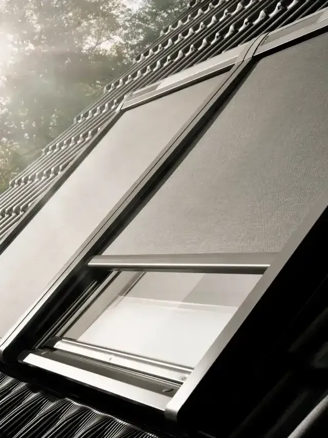 Open skylight window on a slanted roof, with sunlight and trees reflecting on the glass.