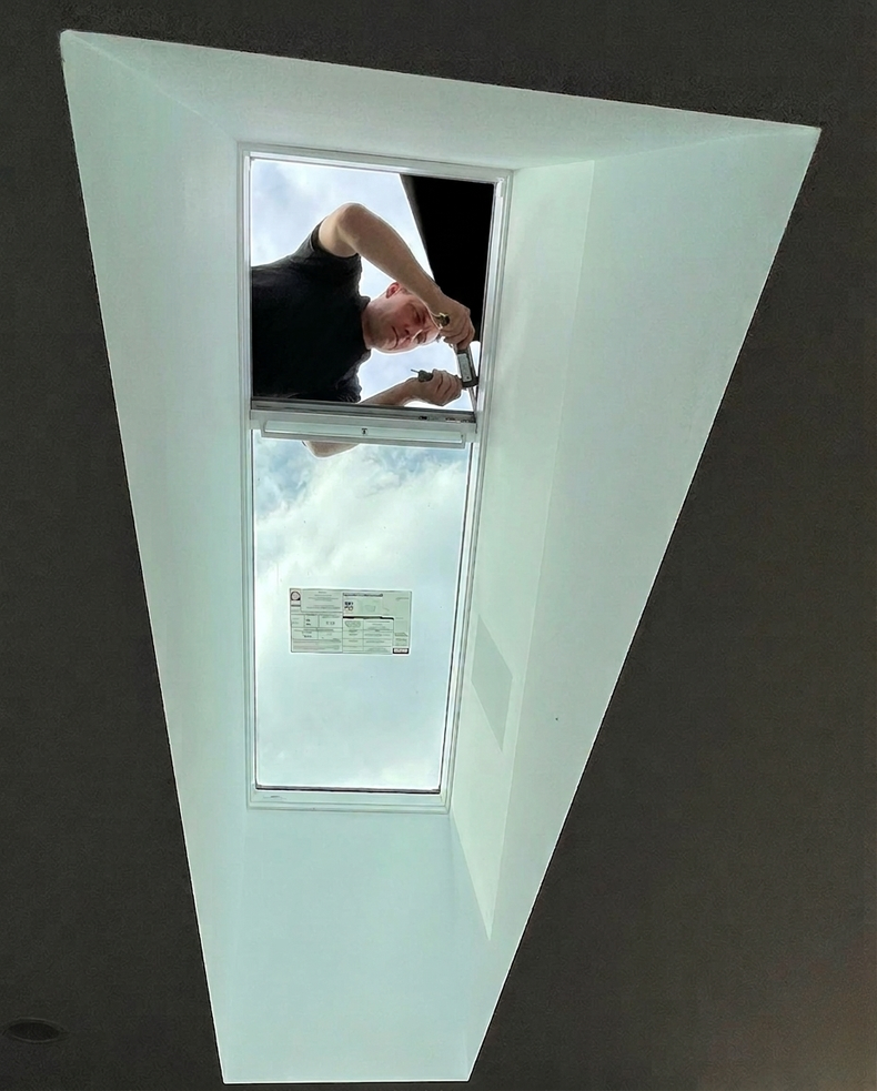 Person reaching through a ceiling access hatch in a white panel on a dark ceiling.