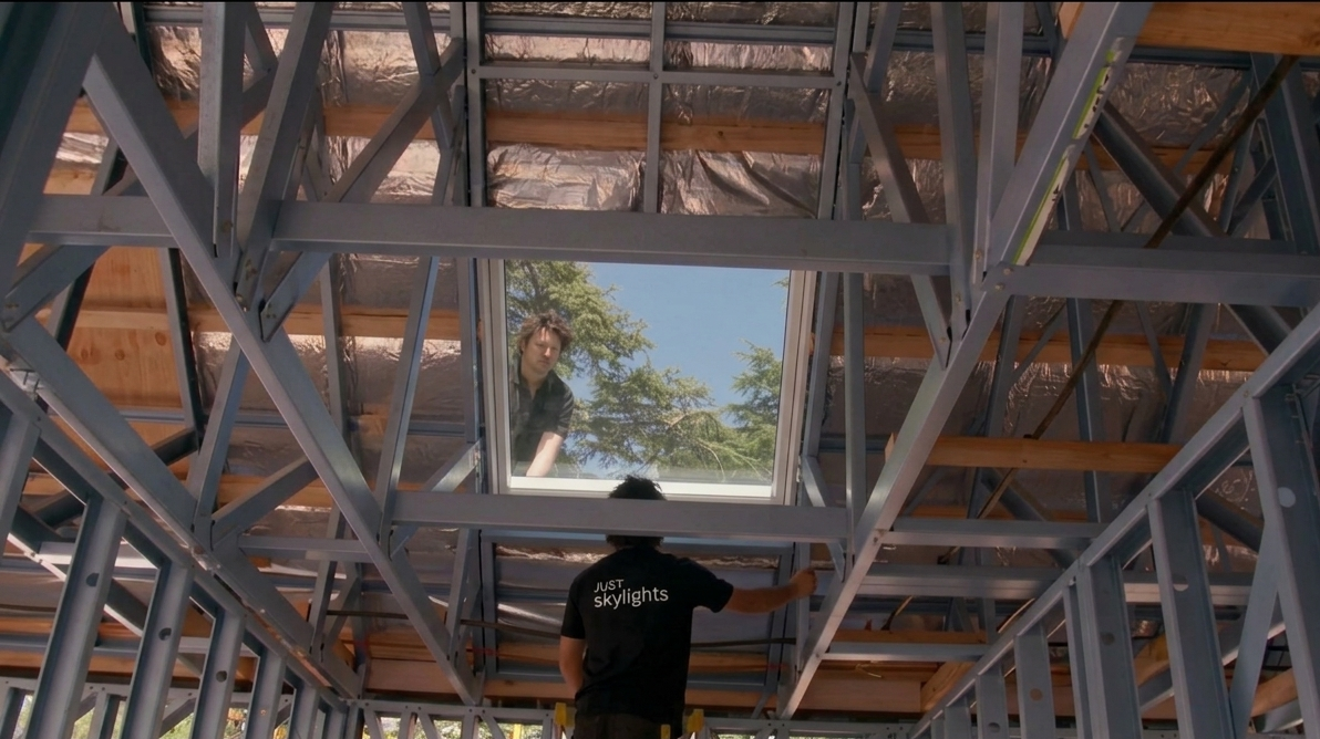 Person standing beneath a metal framework looking up at a skylit ceiling opening
