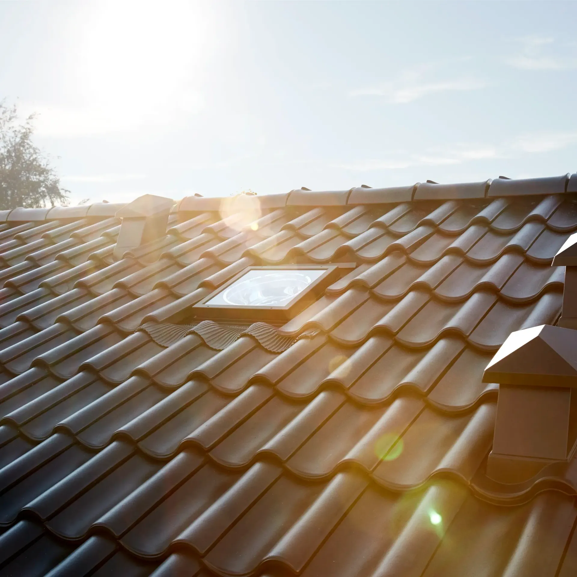 Sunlit terracotta roof tiles with lens flare against a bright sky