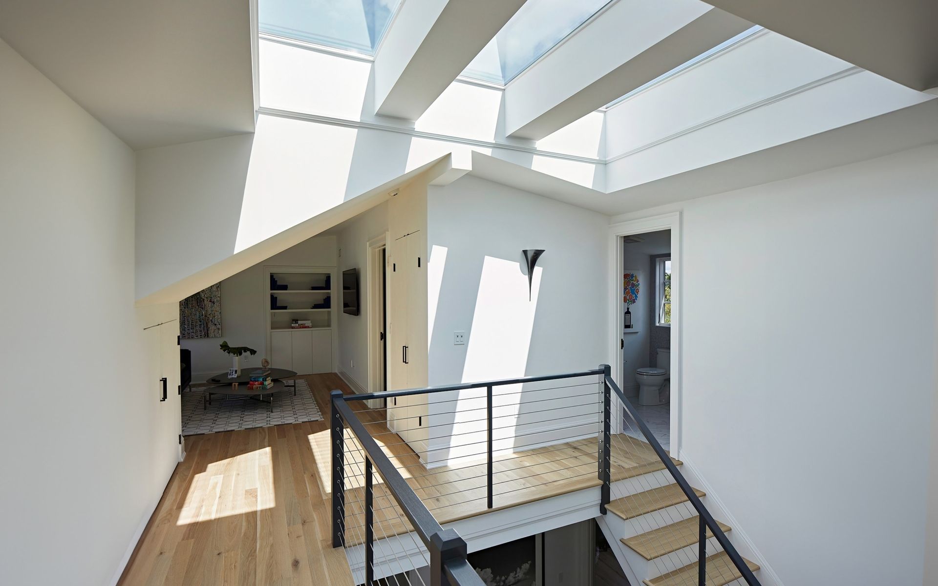 Modern white interior with skylights, loft opening, stairs, and metal railing overlooking a lower level.