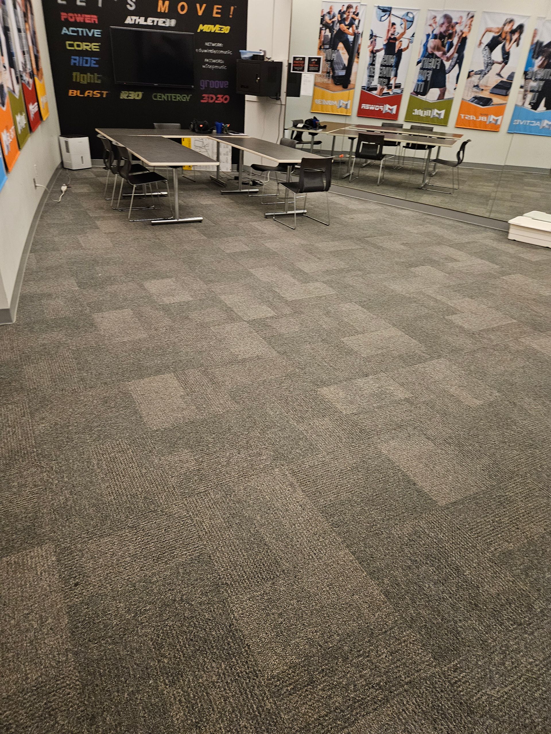 Empty trade show booth with gray carpet, folding tables, and posters on the walls